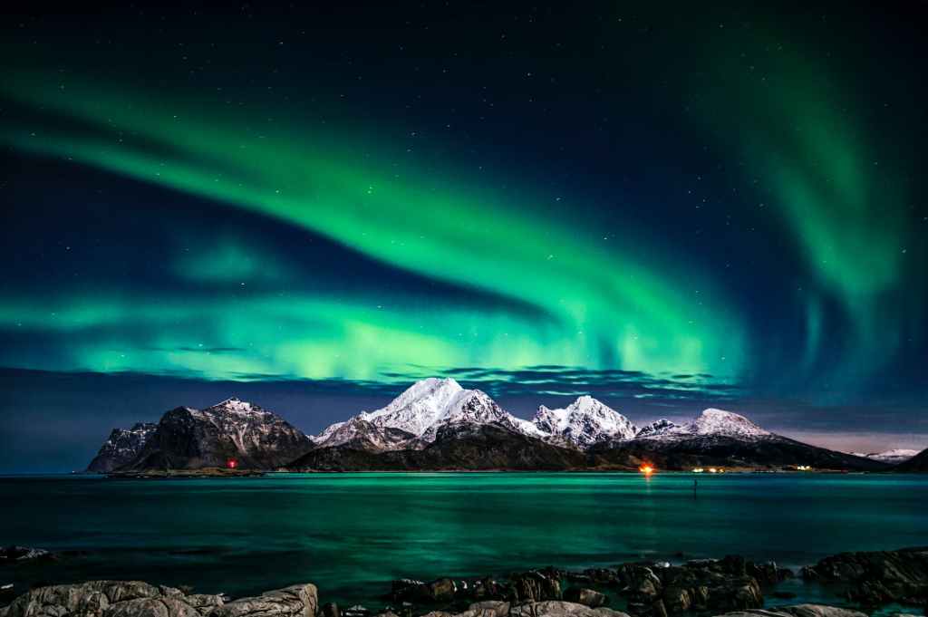 Northern lights over see bounded by snow capped mountains